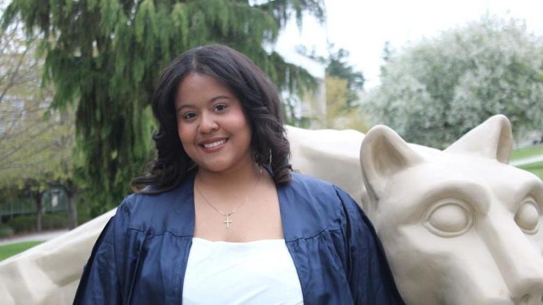 Aidee Santos Acosta poses in front of Nittany Lion Statue in grad gown