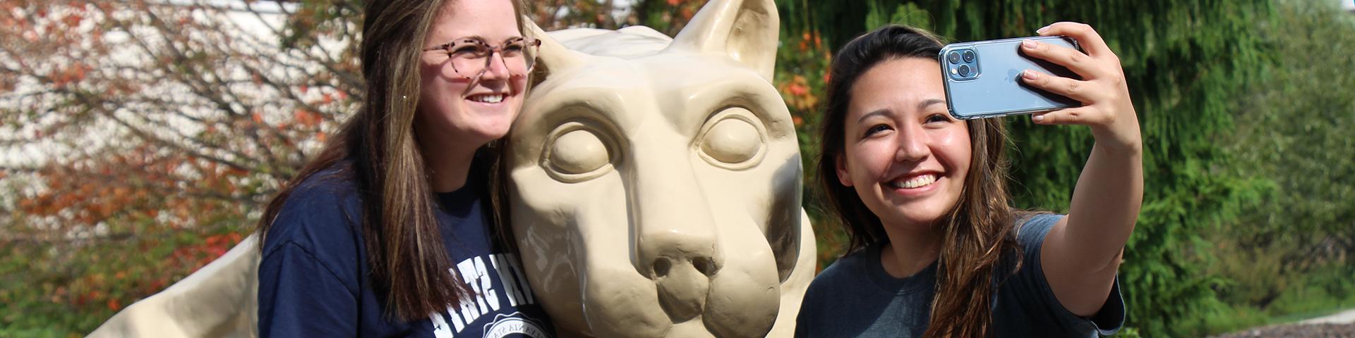 Two female Alumni taking photos with the Nittany Lion Shrine